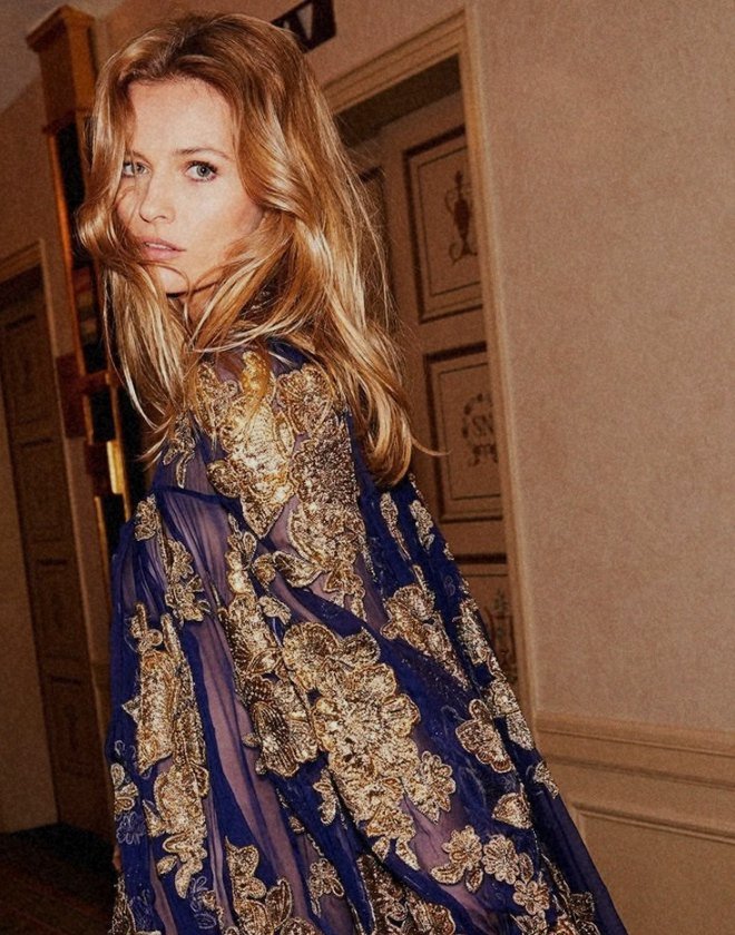 Model in a blue and gold embroidered dress in a hotel hallway